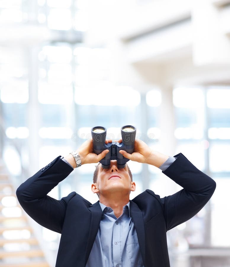 Joven empresario buscando arriba a través de prismáticos mientras de pie en oficina.