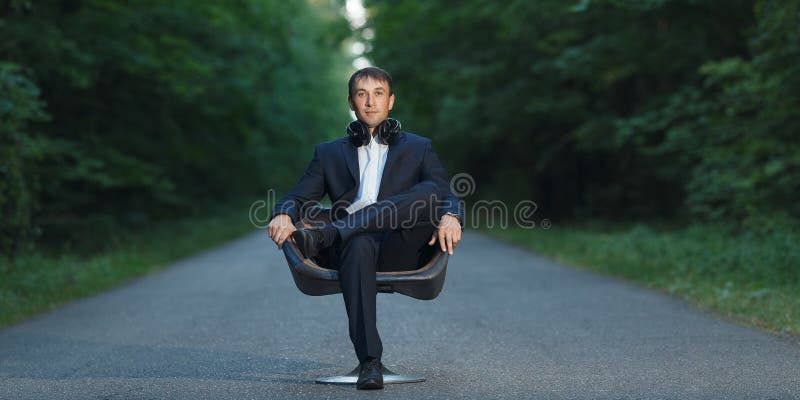 Young business man sitting on chair in suit and headphones in forest royalty free stock photo Young business man sitting on chair in suit and headphones in forest royalty free stock photo