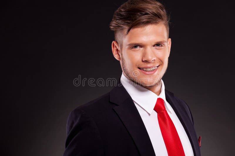 Closeup picture of a young business man looking into the camera with a big smile on his face, revealing braces. on dark background. Closeup picture of a young business man looking into the camera with a big smile on his face, revealing braces. on dark background