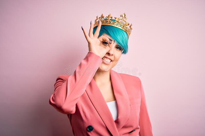 Young business woman with blue fashion hair wearing queen crown over pink isolated background doing ok gesture with hand smiling