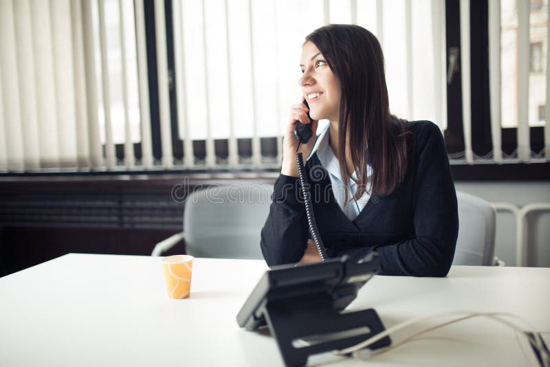 Young business woman calling and communicating with partners.Customer service representative on the phone.Cheerful secretary answering phone in her office and drinking coffee