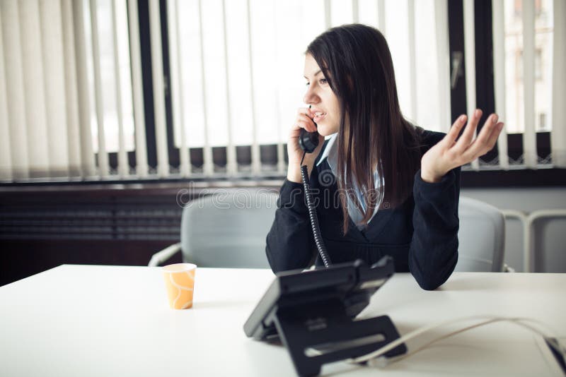 Young business woman calling and communicating with partners. Customer service representative on the phone. Cheerful secretary answering phone in her office and drinking coffee
