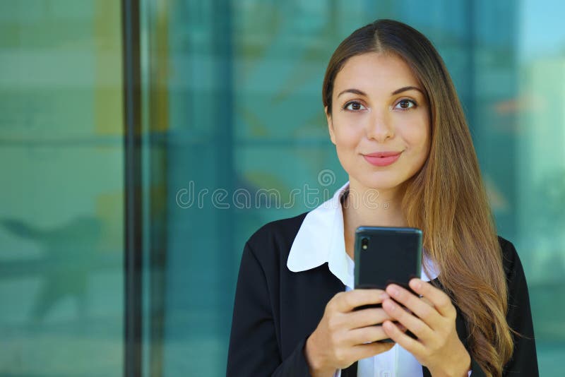 Young business woman checking her smart phone and looking at camera out of office. Copy space royalty free stock photography Young business woman checking her smart phone and looking at camera out of office. Copy space royalty free stock photography