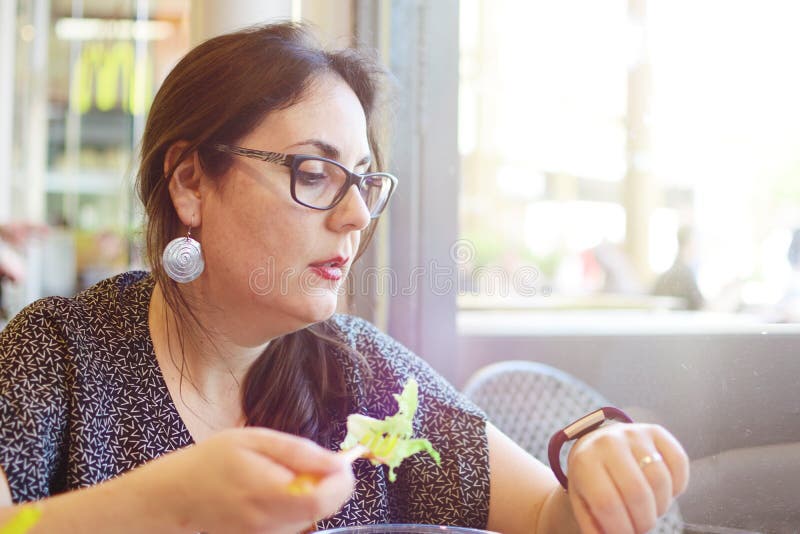 Young business woman at lunch time in the restaurant eating salad and looking at the smart watch counting calories. royalty free stock photo Young business woman at lunch time in the restaurant eating salad and looking at the smart watch counting calories. royalty free stock photo
