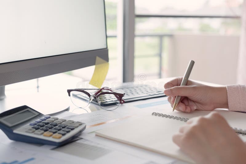 Young business woman sitting at table and taking notes in notebook.On table is laptop