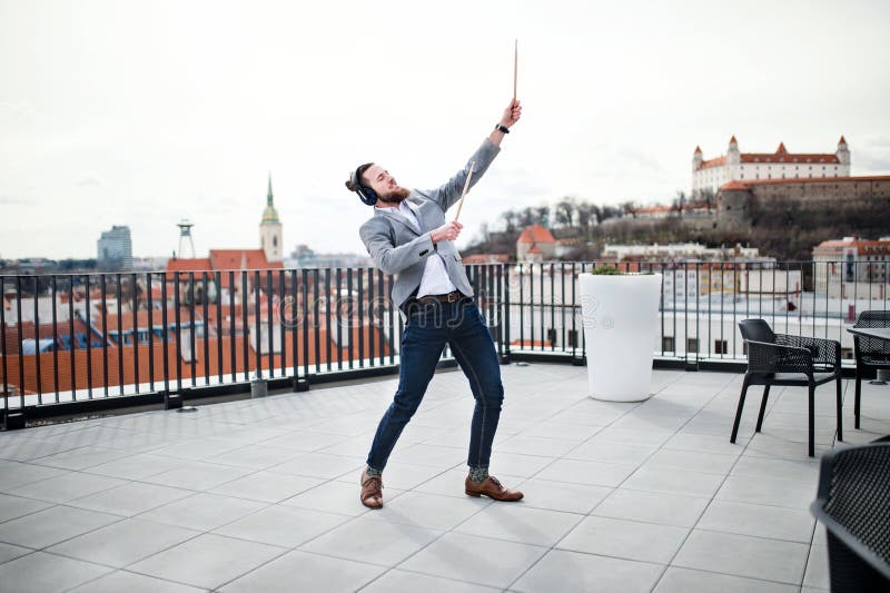 A young businessman with headphones standing on a terrace, having fun.