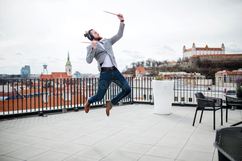 A young businessman with headphones standing on a terrace, having fun.