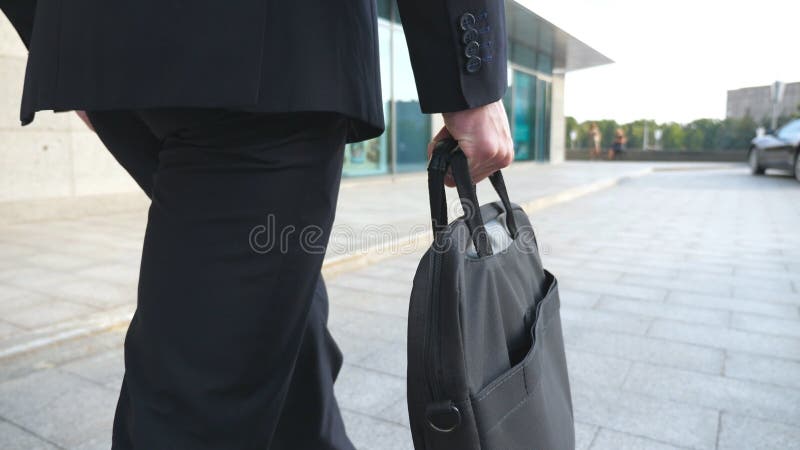 Young businessman holding briefcase in hand and walking in city. Business man commuting to work. Confident guy in suit