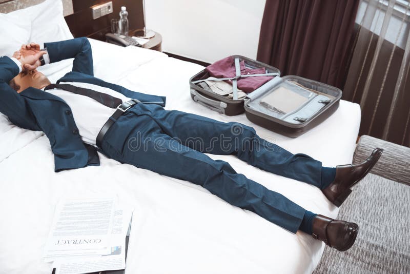 Young businessman lying on bed in hotel room with hands covering royalty free stock photos Young businessman lying on bed in hotel room with hands covering royalty free stock photos