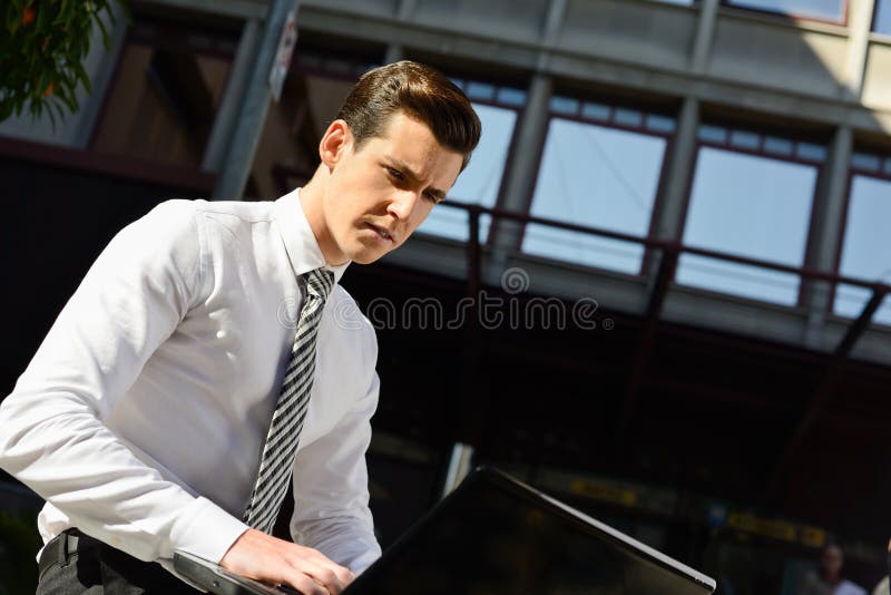 Young businessman typing in a laptop computer in urban background