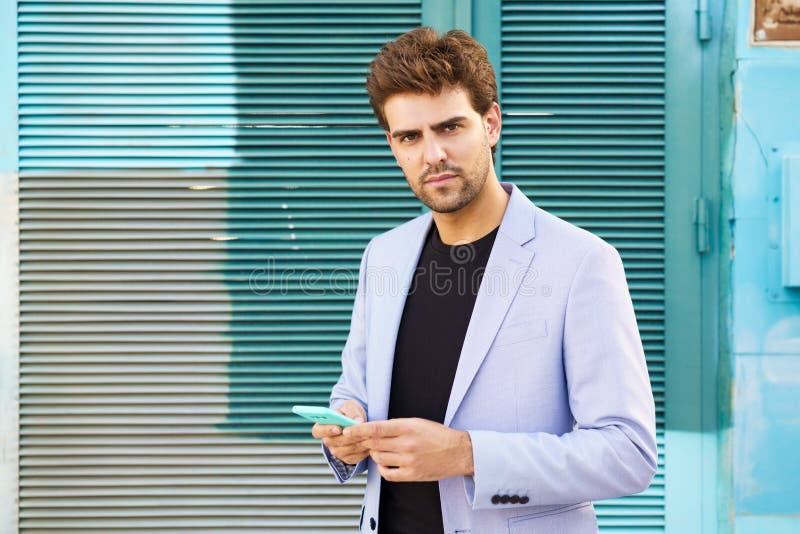 Young businessman wearing blue suit using a smartphone in urban background.