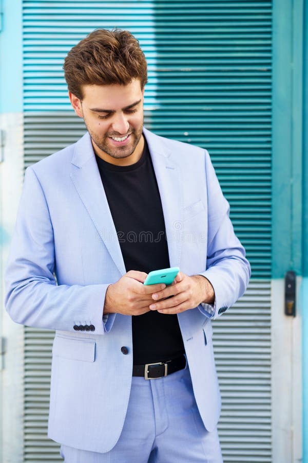 Young businessman wearing blue suit using a smartphone in urban background.