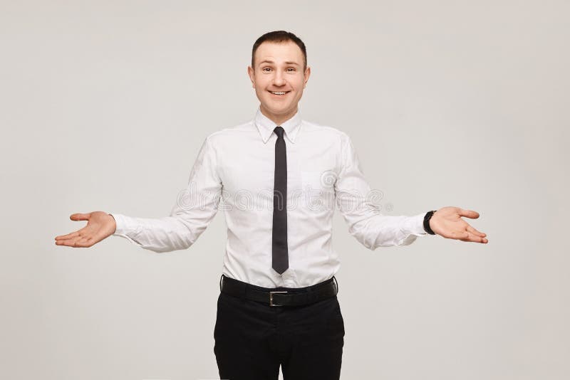 Young businessman in a white shirt and a black tie with arms spread apart on gray background. Isolated with copyspace