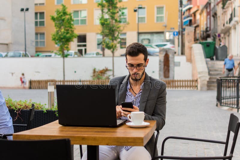 Young businessman is working in a bar terrace with his laptop and smartphone royalty free stock image Young businessman is working in a bar terrace with his laptop and smartphone royalty free stock image
