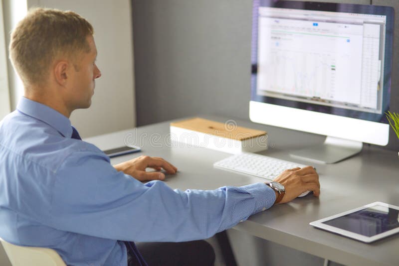Young businessman working in office, sitting at desk, looking at laptop computer screen, smiling royalty free stock photo