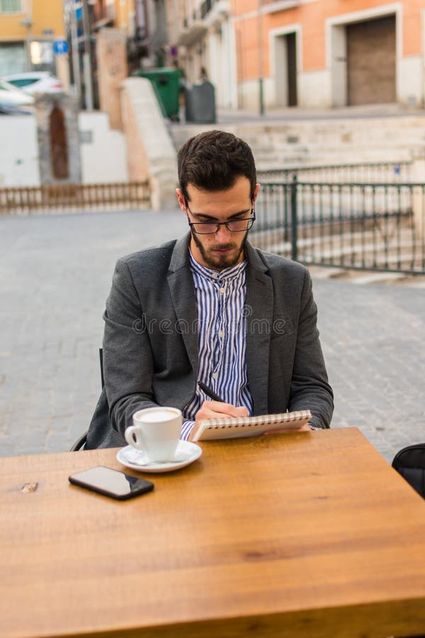 Young businessman is writing in his notebook in a bar terrace royalty free stock images Young businessman is writing in his notebook in a bar terrace royalty free stock images