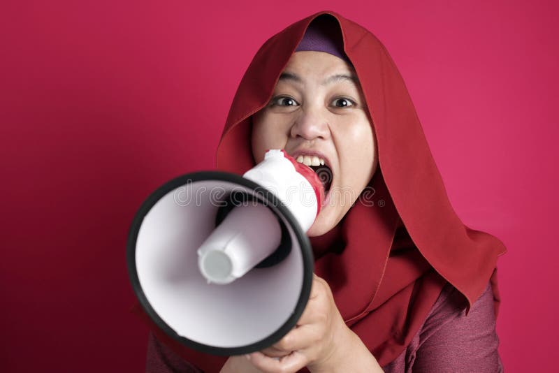 Young Asian muslim businesswoman wearing hijab screaming with megaphone, angry expression. Close up body portrait. Young Asian muslim businesswoman wearing hijab screaming with megaphone, angry expression. Close up body portrait