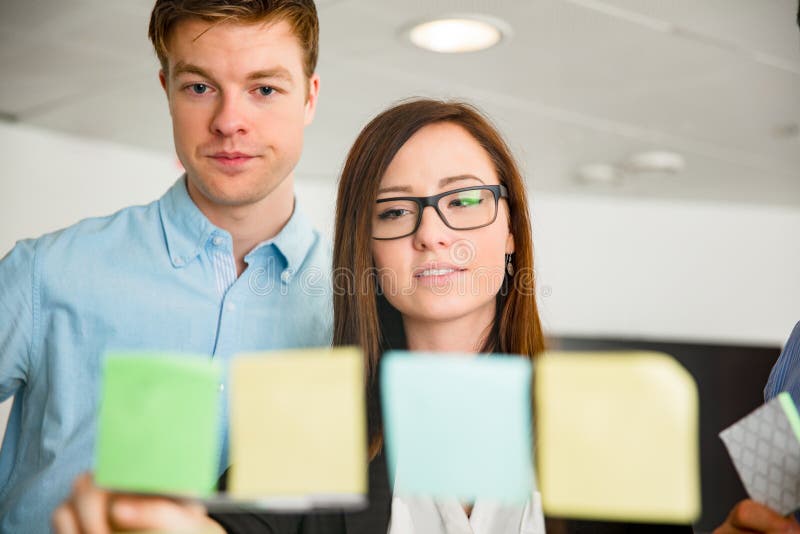 Businesswoman And Colleague Looking At Notes Stuck On Glass royalty free stock images Businesswoman And Colleague Looking At Notes Stuck On Glass royalty free stock images