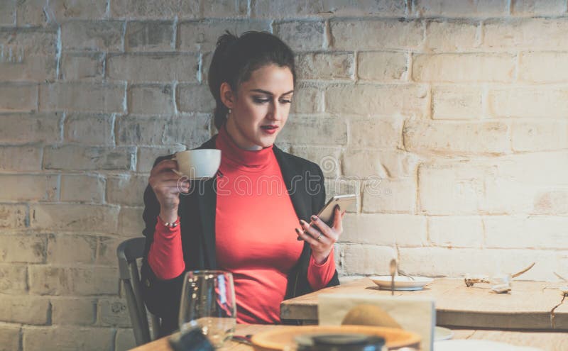 Young businesswoman sitting in cafe at wooden table, drinking coffee and using smartphone. royalty free stock photos Young businesswoman sitting in cafe at wooden table, drinking coffee and using smartphone. royalty free stock photos