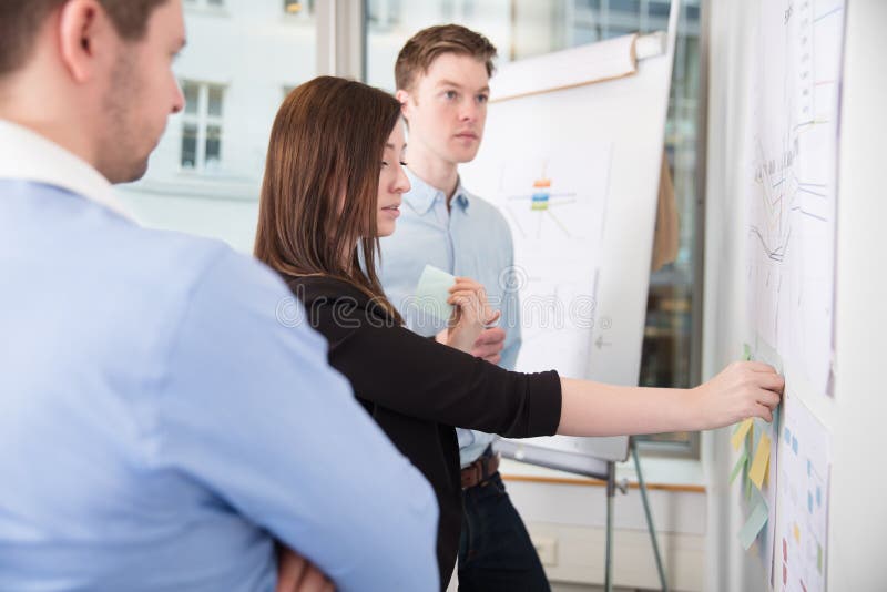Businesswoman Sticking Notes While Standing By Male Colleagues stock photos Businesswoman Sticking Notes While Standing By Male Colleagues stock photos