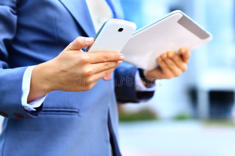 Young businesswoman using digital tablet and mobile phone over building background