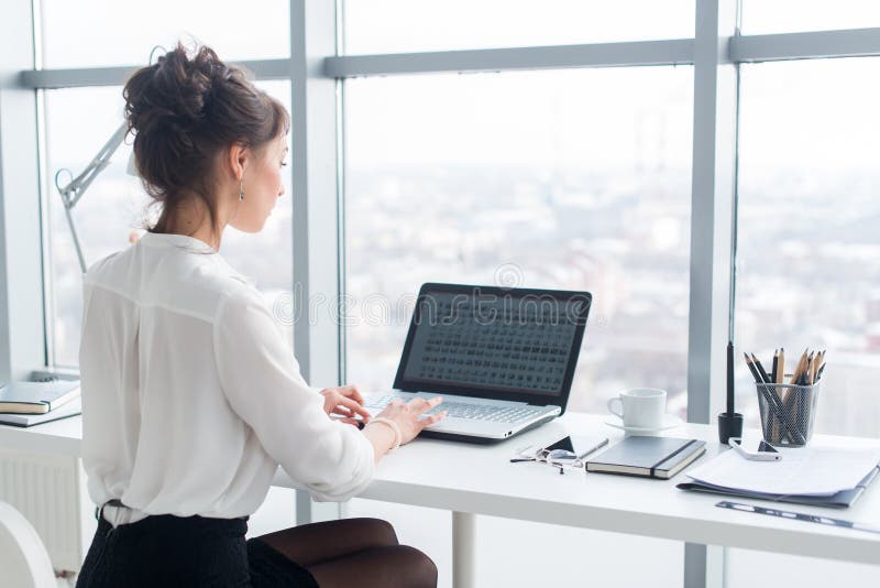 Young businesswoman working in office, typing, using computer. Concentrated woman searching information online, rear