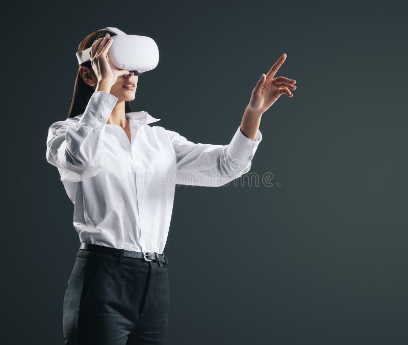 Young businesswoman working in virtual reality environment in VR glasses, presses by her finger on virtual interface on abstract