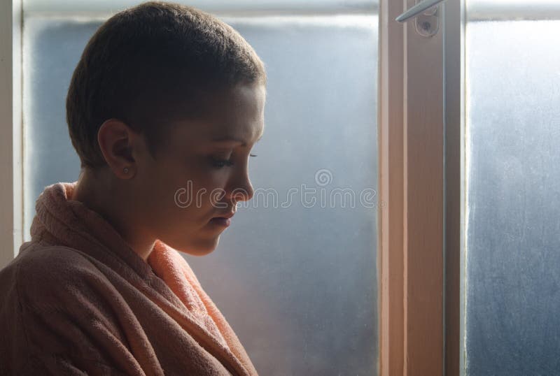 Young cancer patient standing in front of hospital window
