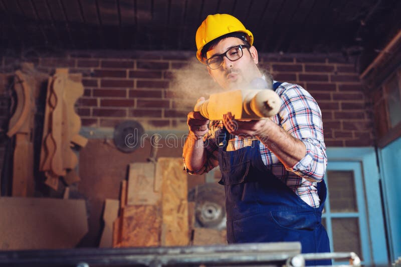 Carpenter blowing sawdust off wooden furniture part