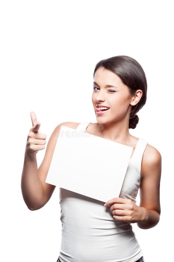 Studio portrait of young attractive casual brunette caucasian female girl holding blank white sign and pointing at camera with index finger with funny expression on her face isolated on white professional makeup hairstyle and retouching. Studio portrait of young attractive casual brunette caucasian female girl holding blank white sign and pointing at camera with index finger with funny expression on her face isolated on white professional makeup hairstyle and retouching