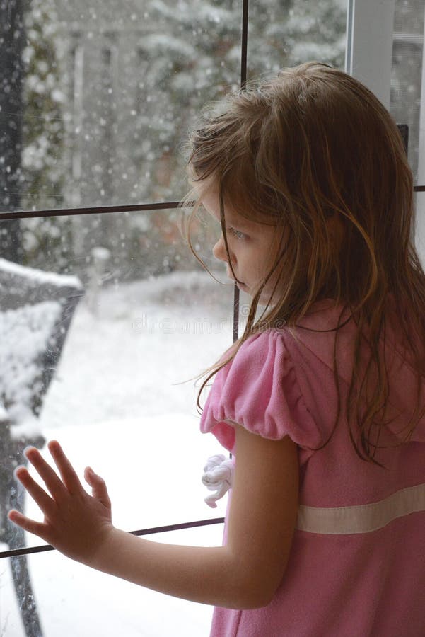 The young Caucasian blonde girl leans on the french glass door and looks at the falling snowflakes outside. royalty free stock photos The young Caucasian blonde girl leans on the french glass door and looks at the falling snowflakes outside. royalty free stock photos