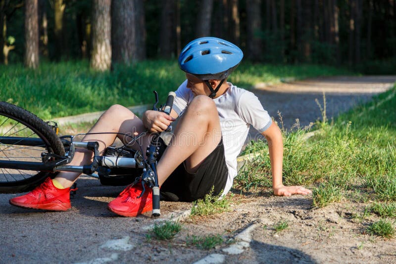Young caucasian boy in helmet and white t shirt got accident and sits on the ground after falling from the bicycle and feels pain royalty free stock image Young caucasian boy in helmet and white t shirt got accident and sits on the ground after falling from the bicycle and feels pain royalty free stock image