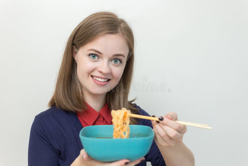 Smiling young woman eating noodles in kitchen stock photo