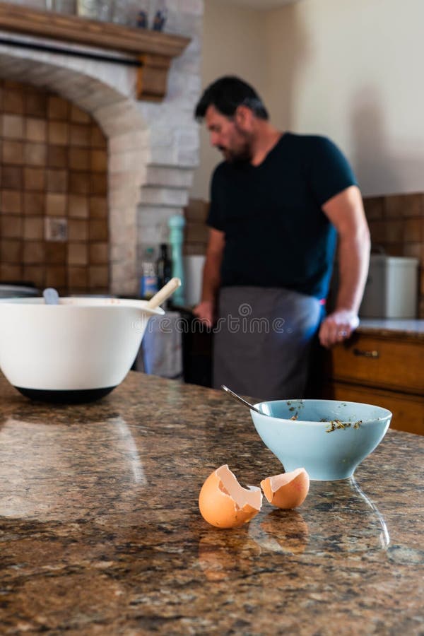 Cooking utensils and ingredients in the foreground and a man in the background leaning on a kitchen worktop. Young Caucasian man baking or cooking in his royalty free stock photography Cooking utensils and ingredients in the foreground and a man in the background leaning on a kitchen worktop. Young Caucasian man baking or cooking in his royalty free stock photography