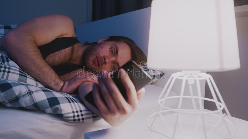 Young caucasian man browsing social media on his phone in the bedroom during the night
