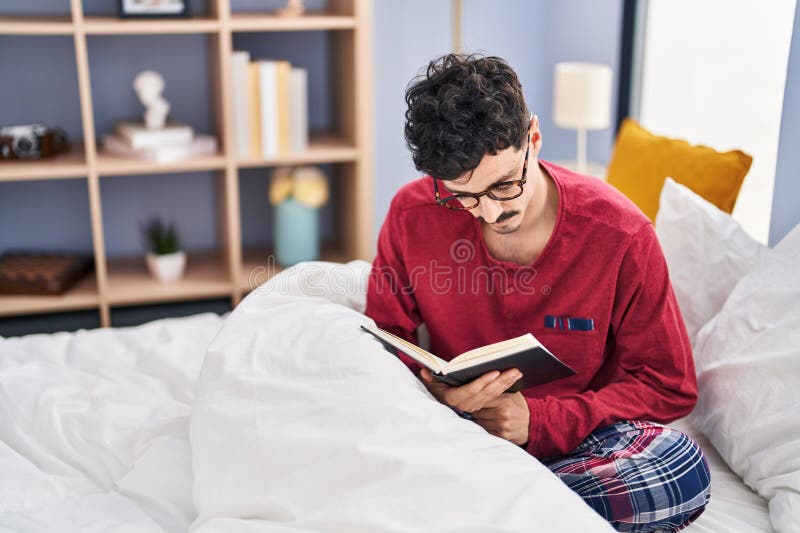 Young caucasian man reading book sitting on bed at bedroom stock images