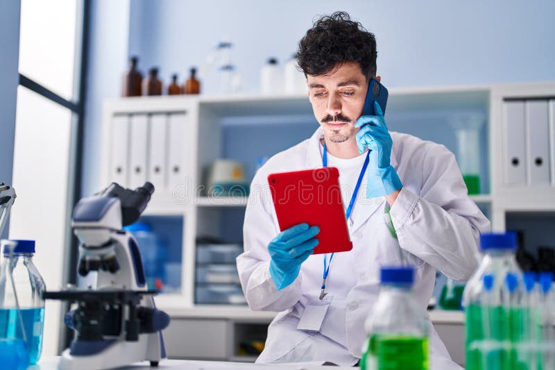 Young caucasian man scientist using touchpad talking on smartphone at laboratory stock photography