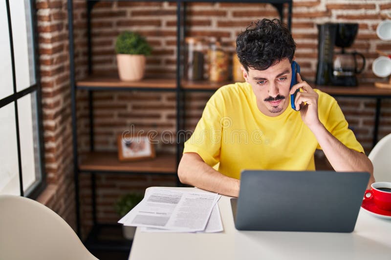 Young caucasian man using laptop talking on smartphone at home royalty free stock photos