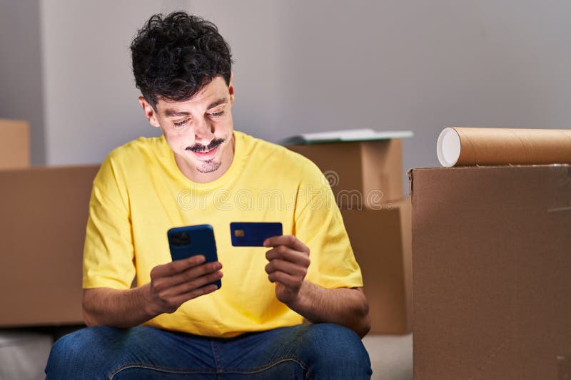 Young caucasian man using smartphone and credit card sitting on sofa at new home royalty free stock photos