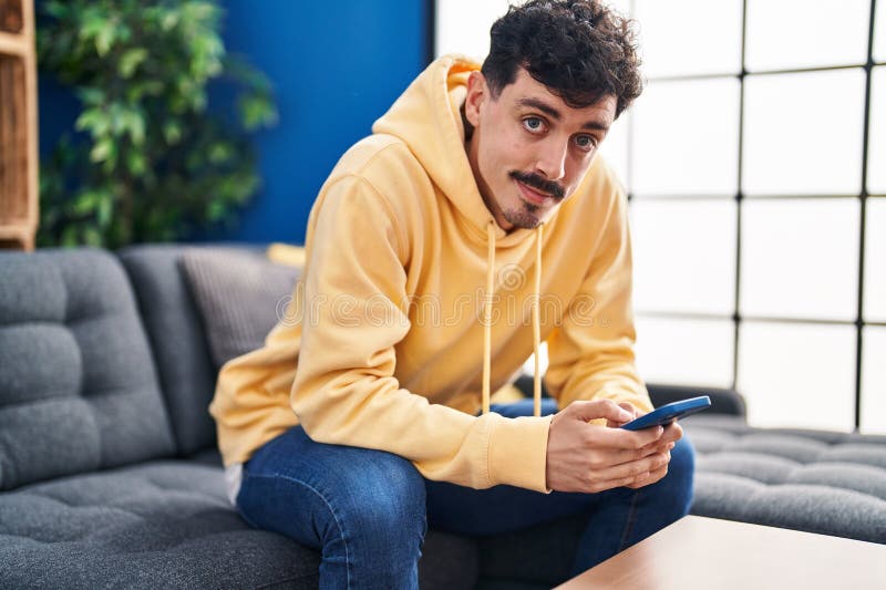 Young caucasian man using smartphone sitting on sofa at home royalty free stock photo