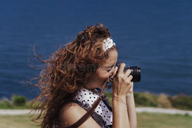 Young caucasian tourist woman outdoors taking pictures with a reflex camera on a windy and sunny day. Lifestyle, travel and royalty free stock photo Young caucasian tourist woman outdoors taking pictures with a reflex camera on a windy and sunny day. Lifestyle, travel and royalty free stock photo