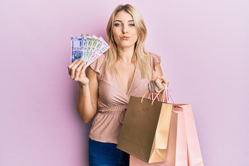 Young caucasian woman holding indian rupee banknotes and shopping bags looking at the camera blowing a kiss being lovely and sexy