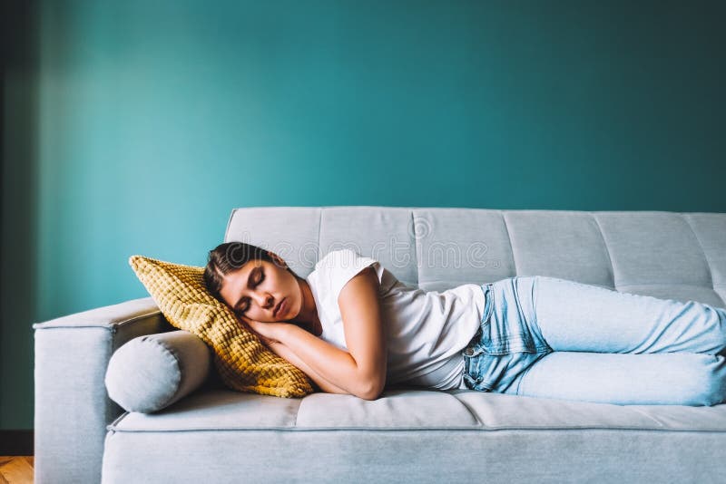 Young Woman Lying on Sofa in Living Room Sleeping after Hard working