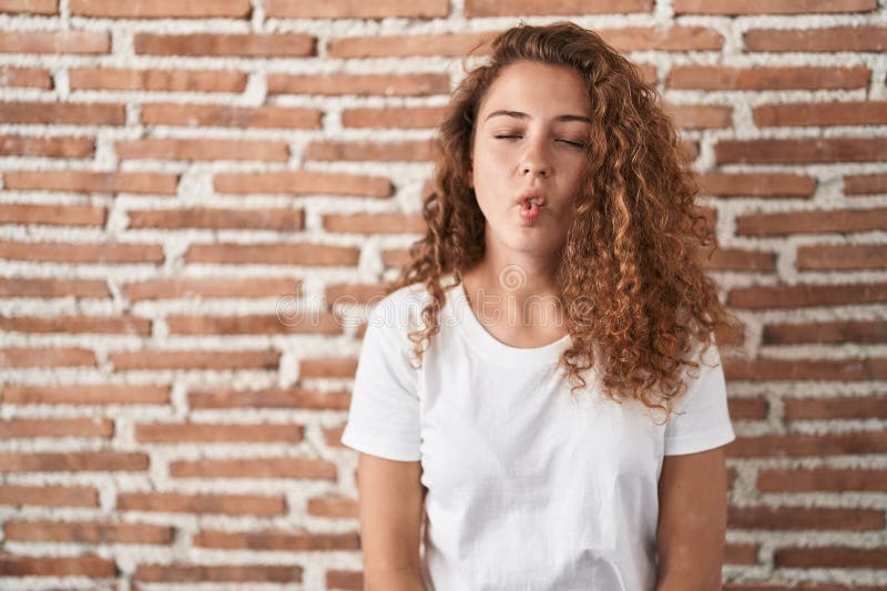 Young caucasian woman standing over bricks wall background making fish face with lips, crazy and comical gesture stock image