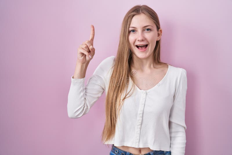 Young caucasian woman standing over pink background pointing finger up with successful idea