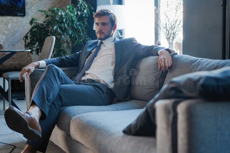Young and charming businessman is thinking about business while sitting on the sofa in his modern office. royalty free stock images Young and charming businessman is thinking about business while sitting on the sofa in his modern office. royalty free stock images