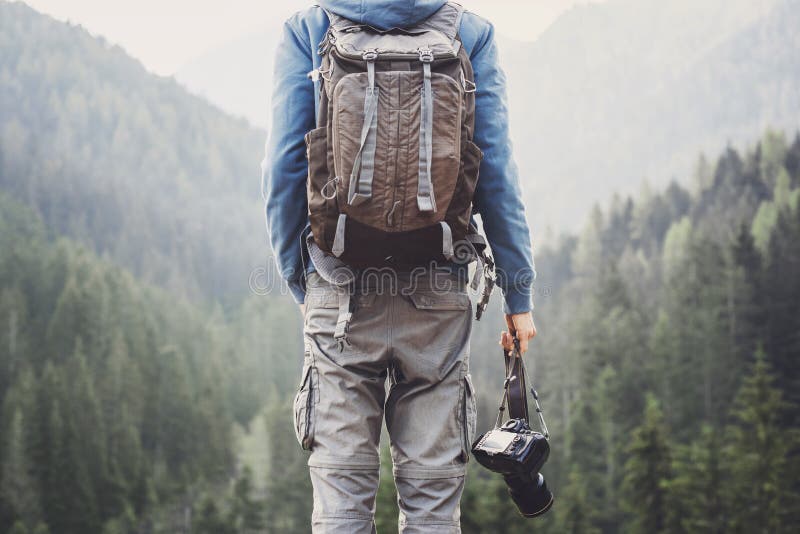 Young cheerful man photographer holding digital camera in a mountains. Photography, travel and active lifestyle c