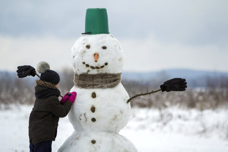Young child boy finish doing smiling snowman in bucket hat, scarf and gloves on empty winter field landscape and clear blue sky co royalty free stock photo Young child boy finish doing smiling snowman in bucket hat, scarf and gloves on empty winter field landscape and clear blue sky co royalty free stock photo