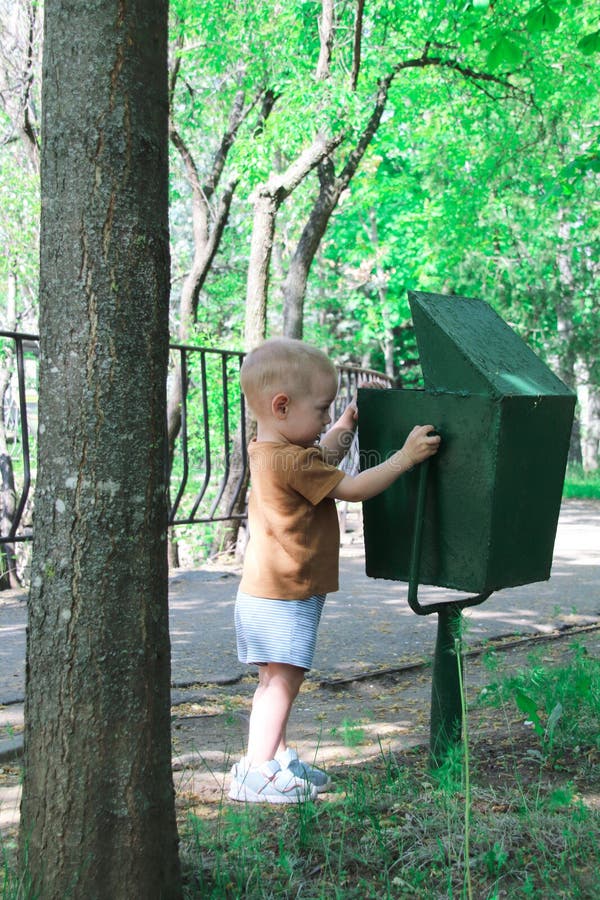 A kid looks at a green trash can in a park. Concept of environmental protection royalty free stock photo