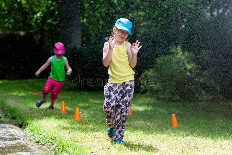 Young children and summer outdoor family activities. Two laughing sisters, happy primary school girls playing outside sprayed by